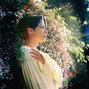 Photo de l'artiste Fatima Al Qadiri en plein air adossée sur des arbustes en fleur