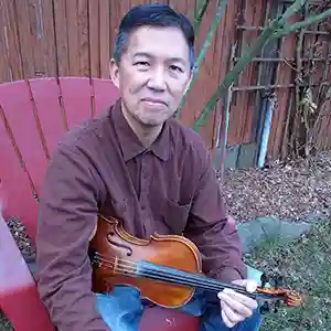 Photo de l'artiste américain Forrest Fang assis dans un fauteuil de jardin avec son violon
