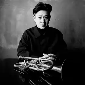 Photo de l'artiste japonais Jun Miyake assis devant son instrument, une trompette.