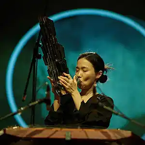 Photo de l'artiste coréenne Park Jiha avec son instrument, le saenghwang, ressemblant à une sculpture en bambou, une sorte d'orgue à bouche.