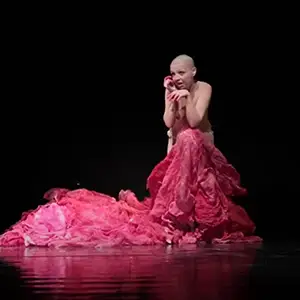 Photo d'une danseuse sur scène dans un costume rouge de Radvilė Juozapaityte dans une pièce de théâtre dansé librement et basée sur le livre de poésie de Jurga Ivanauskaitė "Šokis Dykumoje". Musique : Domantas Balčiūnas