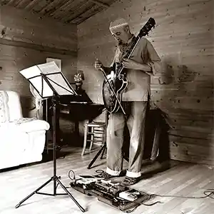 Photo de l'artiste Serge Pesce dans un studio avec sa guitare accommodée et un archet