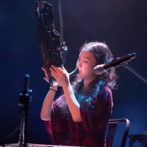 Photo de l'artiste Park Jiha, musicienne coréenne sur scène avec son instrument, un type de hautbois, le saenghwang, ressemblant à une sculpture en bambou, une sorte d’orgue à bouche qui produit un son proche du mélodica.