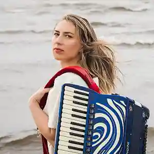 Photo de l'accordéoniste estonienne Tuulikki Bartosik sur une plage au bord de la mer avec son accordéon