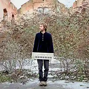 Photo de l'artiste Akamatsu (Rémi Quéron) au pied d'an batiment abandonné avec un synthétiseur dans ses mains