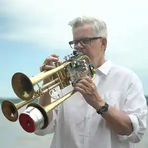 Photo du trompettiste américain Ben Neill dans la nature avec son instrument possédant 6 pistons, trois pavillons et des capteurs.